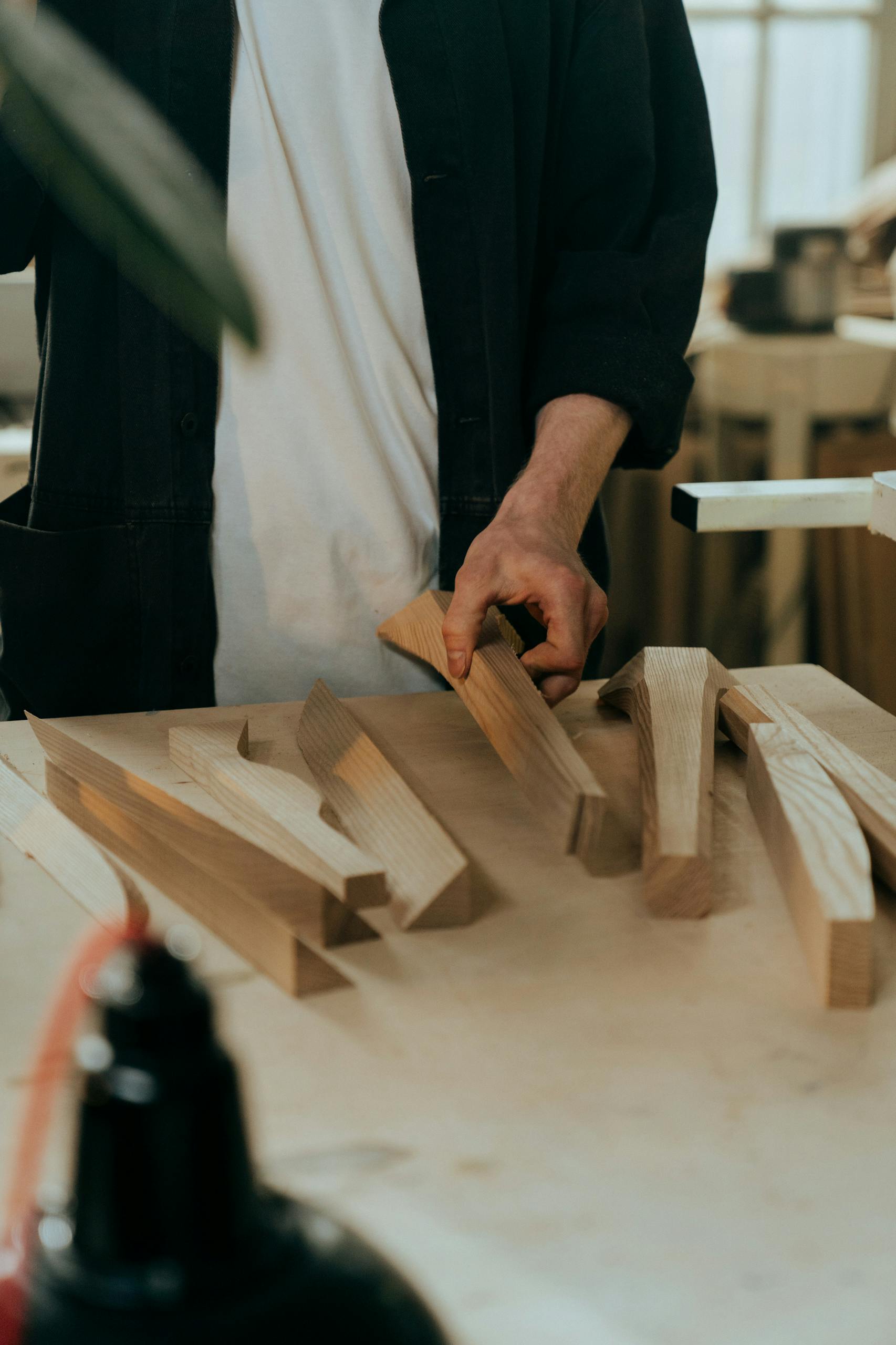 A craftsman choosing wooden pieces for a project in a sunlit workshop.