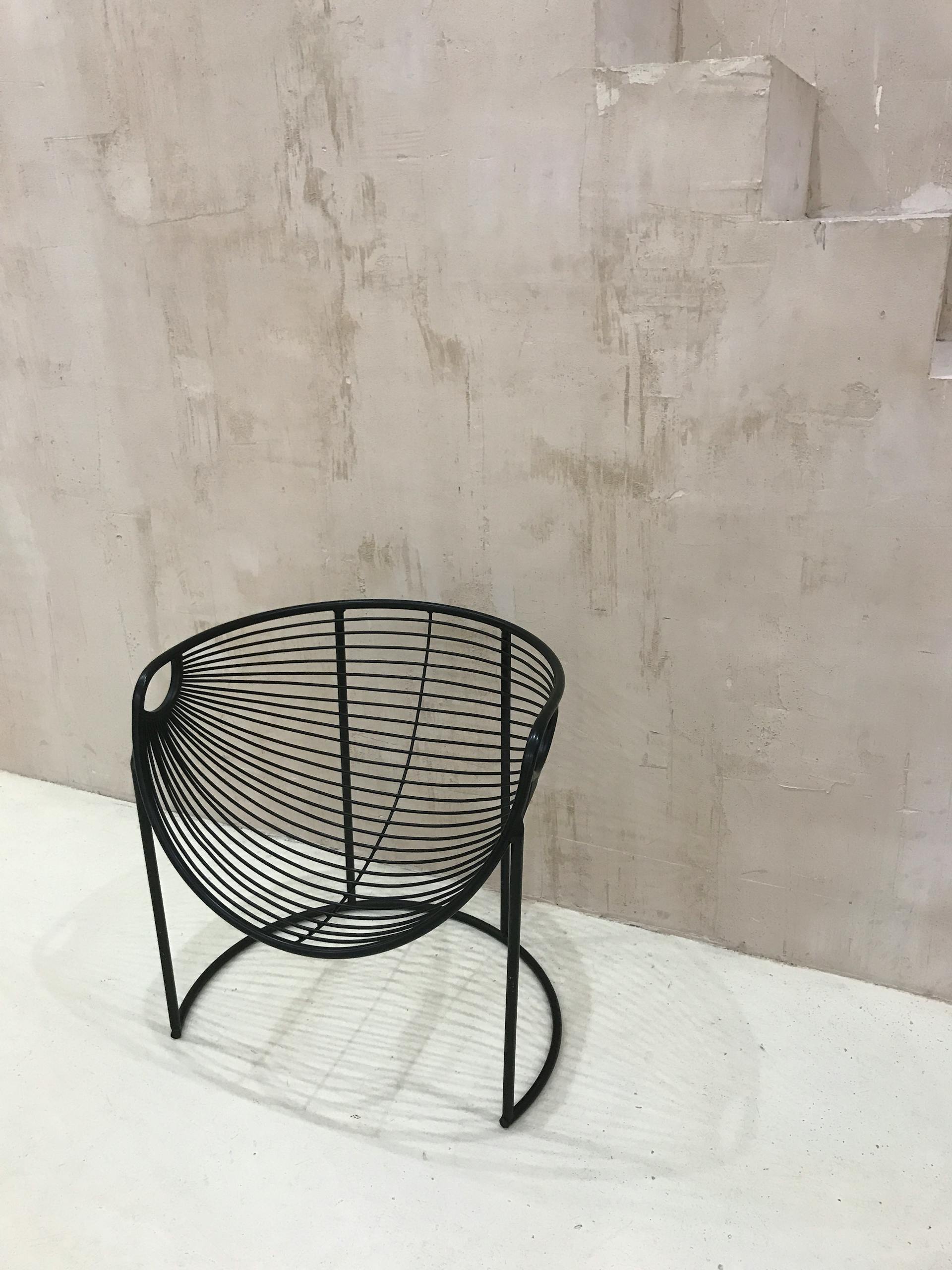 A modern black metal chair placed in front of a textured brown wall on a white floor, showcasing minimalist design.