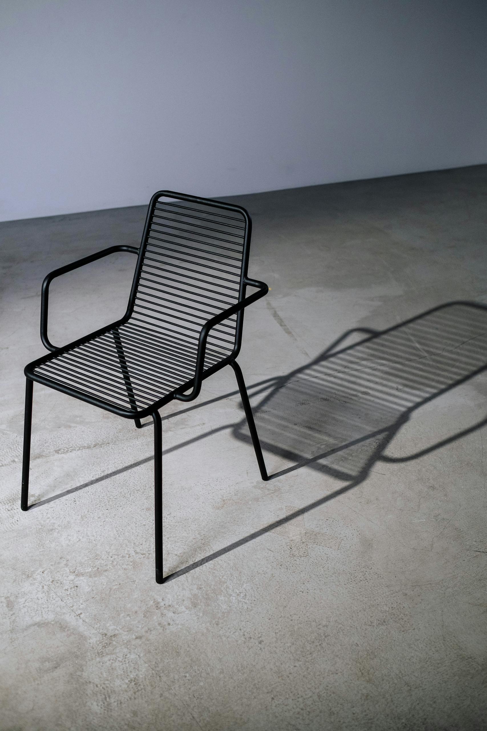 A stylish black metal chair casting a shadow on a concrete floor in a minimalistic setting.